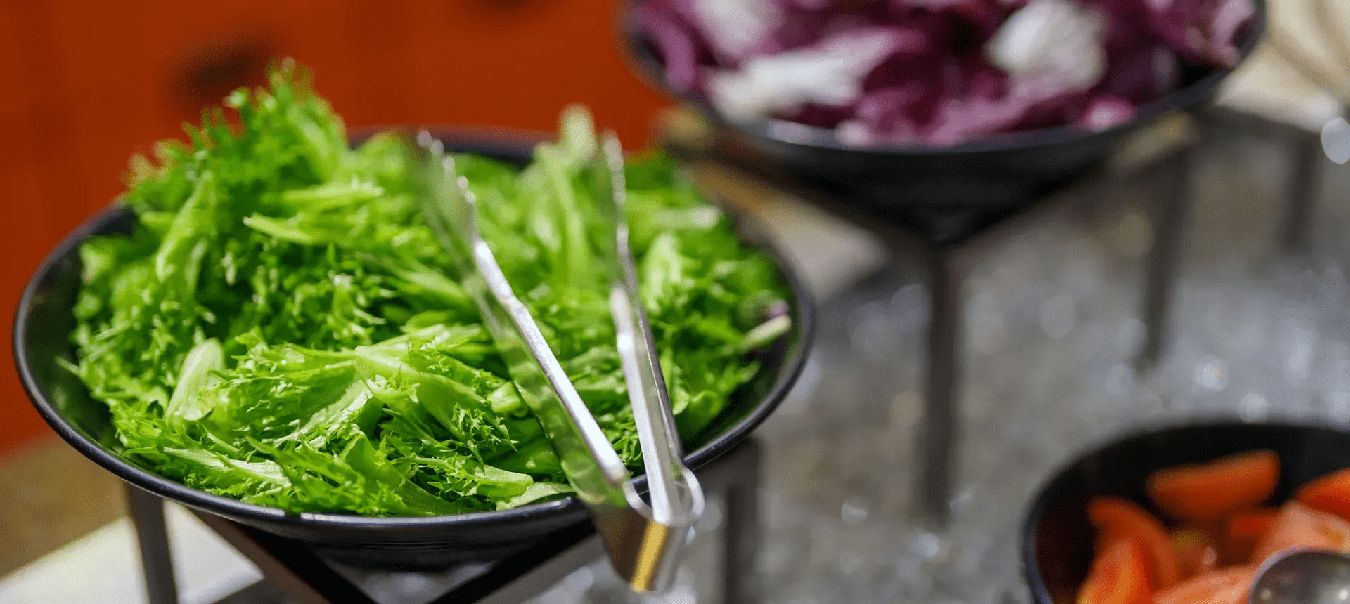 Tongs beside bowl of fresh lettuce leaves